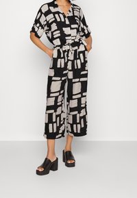Mono negro y crema con estampado, de mangas cortas, cuello, cordón ajustable en la cintura y piernas cortas. Combina con sandalias de plataforma negras.