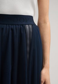 Jupe en tulle navy avec une finition texturée, dotée d'une large ceinture emboutie du logo "JOOP!" et de deux bandes satinées verticales pour le détail.
