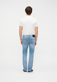 Φωτεινά γαλάζια τζιν παντελόνια με στενή εφαρμογή, μέση μεσαίου ύψους, τέσσερις τσέπες και μαύρη ετικέτα στο πίσω μέρος. Φορεμένα με μια απλή λευκή μπλούζα.