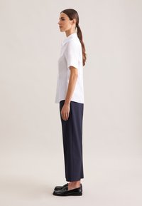 Weißes kurzärmeliges Hemd kombiniert mit marineblauen, zulaufenden Hosen. Das Outfit verfügt über einen klassischen Kragen und schwarze Loafers. Einfaches und sauberes Design.