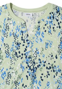Chemise vert clair avec des taches abstraites bleues, noires, blanches et grises et un col rond avec une petite fente à l'avant.