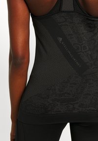 Primer plano de la espalda de una persona que lleva una camiseta deportiva texturizada negra de Adidas by Stella McCartney y leggings a juego.
