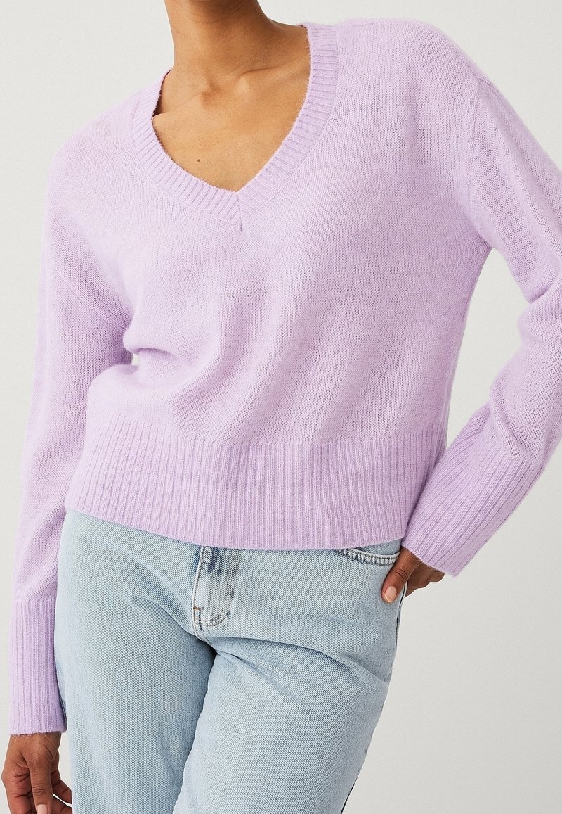 Maglione lilla in maglia leggera con scollo a V, polsini e orlo a costine. Abbinato a un denim azzurro chiaro, con una vestibilità rilassata e una trama visibile.