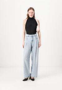Zwarte geplooide mouwloze top, lichtblauwe high-waisted wijde jeans en zwarte hakken; kleine roze tas over de schouder.