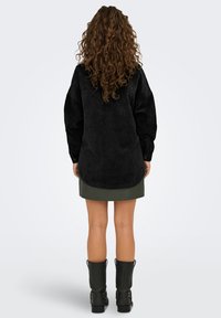 Zwarte fluwelen oversized shirt met een afgeronde zoom, lange mouwen en een zak. Gepaard met een groene leren rok en zwarte enkellaarsjes.