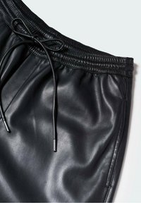 Pantalon en simili cuir noir avec taille élastique et cordon de serrage noué sur fond uni.