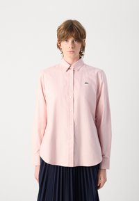 Camicia button-up di cotone rosa chiaro, con colletto classico e un piccolo ricamo di logo verde sul lato sinistro del petto.