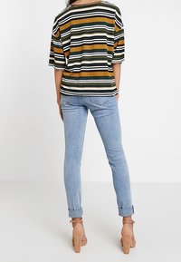Top de tirantes a rayas en verde, amarillo y negro, combinado con jeans skinny de color azul claro y zapatos de tacón beige.