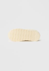 Apavu zole ar teksturētu gumijas virsmu bēšā krāsā, viļņveidīgu rakstu un maziem apļveida izcilņiem saķerei.