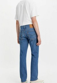 Blå denimjeans med rak passform och ljus tvätt, med bakfickor och en beige läderlapp på bakpanelen.
