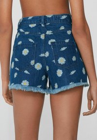 Szorty dżinsowe w niebieski wzór kwiatowy z białymi stokrotkami. Poszarpane krawędzie i podwójne kieszenie z tyłu. Tkanina w ciemnym odcieniu.