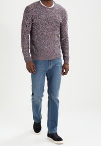 Pull-over en maille texturée avec un motif chiné de nuances rouges et grises, assorti à un jean en denim bleu clair et des baskets noires.