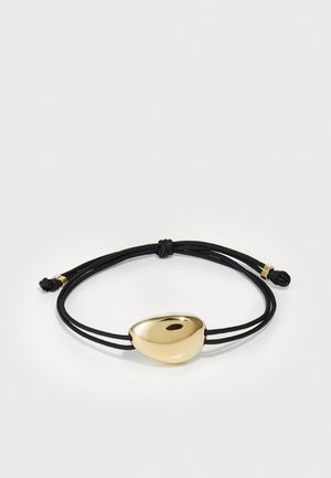 Sort snorarmbånd med en poleret guldfarvet sten som midtpunkt. Har justerbare knuder; glat overflade med subtile reflektioner.