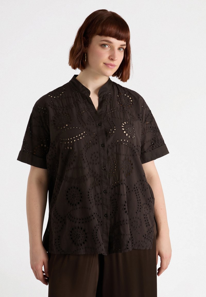 Camicia button-up corta a maniche corte di colore marrone scuro, realizzata in tessuto leggero con motivi tagliati al laser e colletto alla cinese. Dettagli testurizzati in tutto il capo.