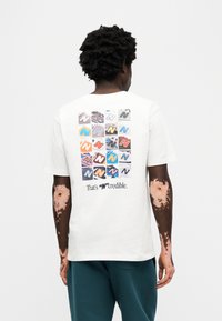 Λευκό βαμβακερό t-shirt με πολύχρωμο γραφικό με λογότυπα "N" στην πλάτη, με κείμενο "That's N'credible" κάτω από το σχέδιο.