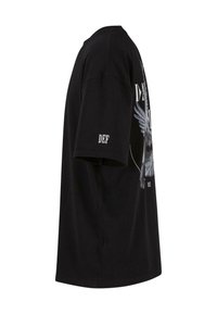 Tricou negru din bumbac cu un design grafic cu aripi și text. Mâneci scurte și guler rotund. Viu lateral arată o croială lejeră.
