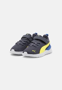 Chaussures de sport grises avec des accents jaunes et bleus, tige en mesh, col rembourré, sangle réglable et semelle blanche avec grip texturé.