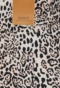 Tecido com padrão de leopardo em preto e creme, com um acabamento texturizado; apresenta um rótulo de couro castanho com texto embossado "ONLY" cosido.