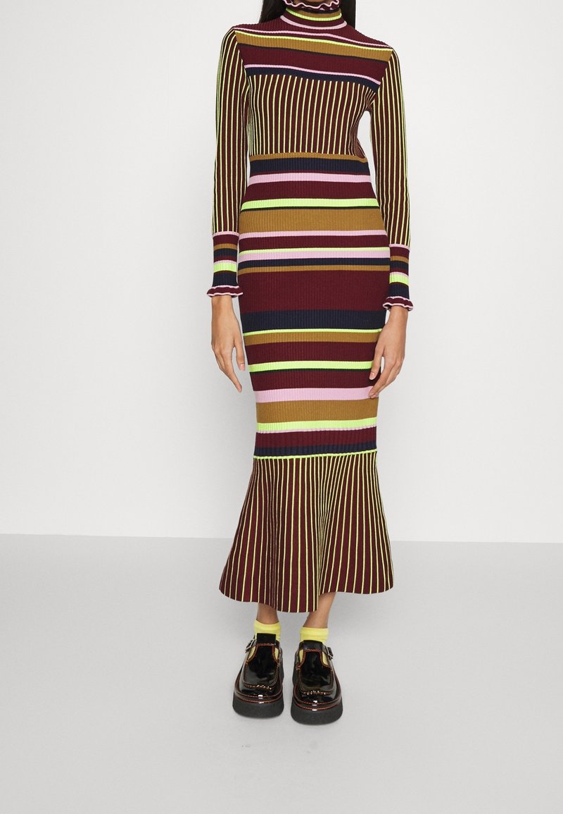 Randig, ribbad trikåklänning med hög krage; färger inkluderar burgundy, olivgrön, rosa och gul. Har en utsvängd fåll och långa ärmar.