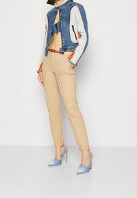 Veste en denim avec manches grises contrastantes et accents orange, pantalon beige et chaussures à talons hauts bleu clair.