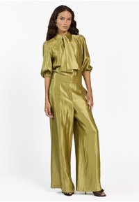 Glanzend olijfgroen twee-delig outfit met een blouse met kraag en strik en wijde broekspijpen. Zachte textuur met een comfortabele pasvorm.