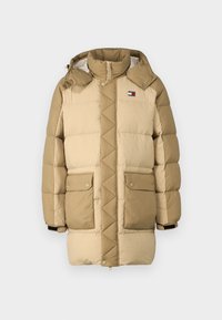 Beige puffjakke med kviltet tekstur, høy krage og to frontlommer. Har en logo-patch på venstre bryst og svarte mansjettaksenter.