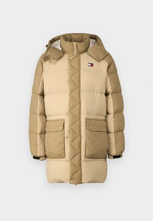 Beige puffer jacket with quilted texture, high collar, and two front pockets. Features a logo patch at the left chest and black wrist accents.
