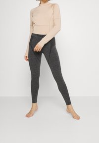 Långärmad beige topp med figurnära, svarta, texturerade leggings som har en hög midja och subtila designinslag.