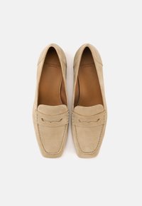 Μπεζ μοκασίνια από σουέτ με ραμμένα σχέδια και μαλακή δερμάτινη επένδυση. Κλασικός σχεδιασμός slip-on με στρογγυλεμένη μύτη και διακριτικά διακοσμητικά στοιχεία.