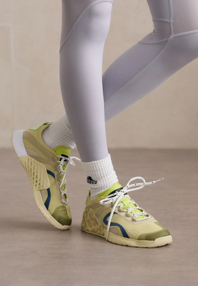 Des chaussures de sport vert clair et beige avec des accents bleus et des panneaux texturés, dotées de lacets blancs et d'un talon rembourré pour le soutien.