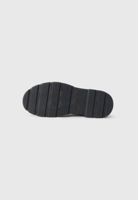 Suola di scarpa in gomma nera con texture rigata e scanalature orizzontali. Profilo piatto con punta arrotondata e leggera curvatura verso l'alto al tallone.