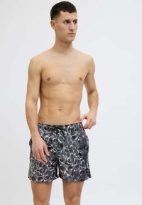 Costumi da bagno neri e grigi con un motivo ad acqua, vita elastica e cordoncino. Realizzati in materiale leggero e ad asciugatura rapida.