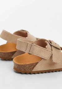 Tan mockasiner i mocka med korkinsats, justerbart ankelband och texturerad sula. Har en enkel och bekväm design.