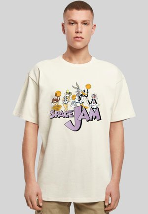 Osoba w białej koszuli z postaciami z filmu "Space Jam" kozłującymi piłki koszykowe powyżej napisów "Space Jam" w purpurze i czerni.