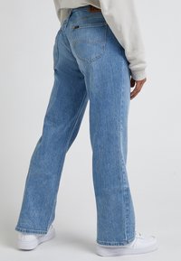 Ljust blå denimjeans med rak benform, kontrasterande sömmar, bakfickor och en beige läderlapp vid midjan.