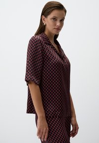 Korte mouwen blouse in donkerrood met een diamantenpatroon in marineblauw en lichtrood. Gemaakt van gladde stof met een ontspannen pasvorm en kraagontwerp.