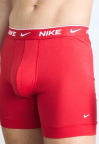 Rode Nike boxershorts met een wit logo op de tailleband en een klein logo op het onderbeen. Glad textuur, aansluitende pasvorm en lengte tot halverwege de bovenbenen.