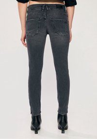 Upnuté tmavě šedé džíny se středním pasem, dvěma zadními kapsami a odřenými detaily, v kombinaci s černými lodičkami na vysokém podpatku.
