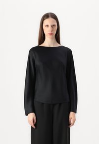 Top lungo maniche in satin nero con scollo a barca, texture liscia e vestibilità morbida, abbinato a pantaloni neri larghi.