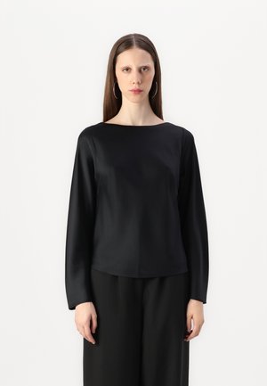 Black satin long-sleeve top with a boat neckline, smooth texture, and relaxed fit, paired with loose black trousers.