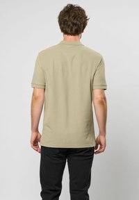 Beige paita polo lyhythihaisella, kauluksella ja teksturoidulla kankaalla; käytössä mustien housujen kanssa, nähty takaa.
