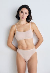 Bralette beige senza cuciture con sottili spalline e coordinati mutandoni a vita alta, caratterizzati da una texture liscia e un design minimalista.
