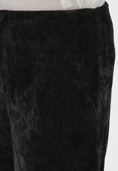 Pantalon en tissu texturé noir avec une apparence douce et veloutée, doté de poches latérales et d'une ceinture élastique pour le confort.