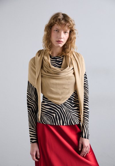 Sciarpa beige appoggiata su una maglietta a righe bianche e nere, abbinata a una gonna di raso rossa fluida. Le texture lisce e i colori a contrasto sono evidenti.