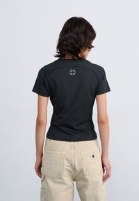 Schwarzes T-Shirt mit kurzen Ärmeln und grünen Akzentdetails. Mit Rundhalsausschnitt und kleinem Logo auf der Rückseite. Glattes, figurnahes Design.