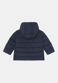 Marineblauw pufferjack met capuchon, horizontaal doorgestikt ontwerp en lange mouwen. Soepele textuur zonder zichtbare sluitingen of versieringen.