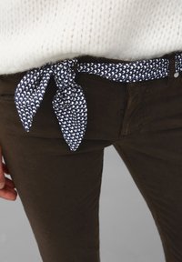 Pantaloni marroni con una cintura a righe blu navy con forme bianche, abbinati a un maglione crema strutturato. Viste ravvicinate dei dettagli dell'outfit.