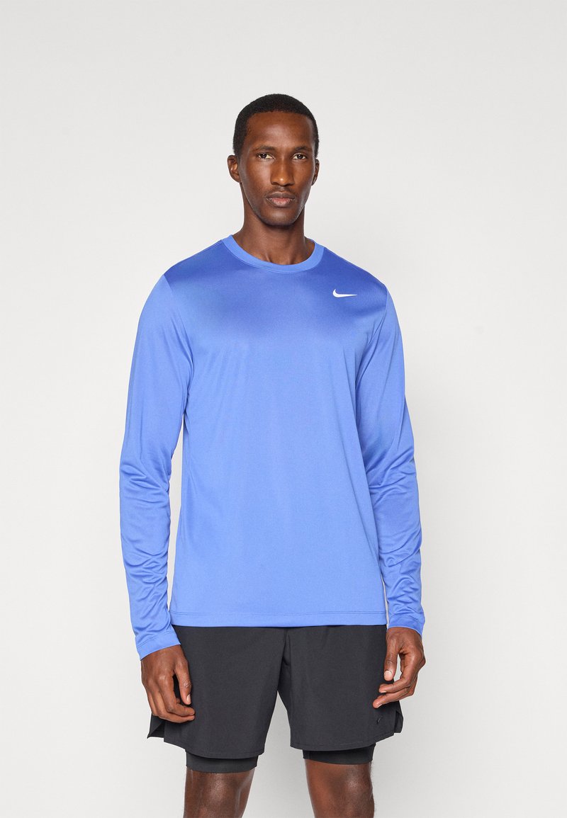 Langærmet blå træningsskjorte lavet af syntetisk stof, med rund hals og et hvidt Nike-logo på venstre side af brystet.