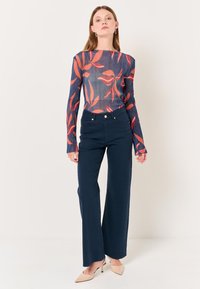 Top a maniche lunghe, trasparente, con motivo floreale rosso su sfondo blu navy, abbinato a pantaloni blu navy a vita alta e tacchi beige.