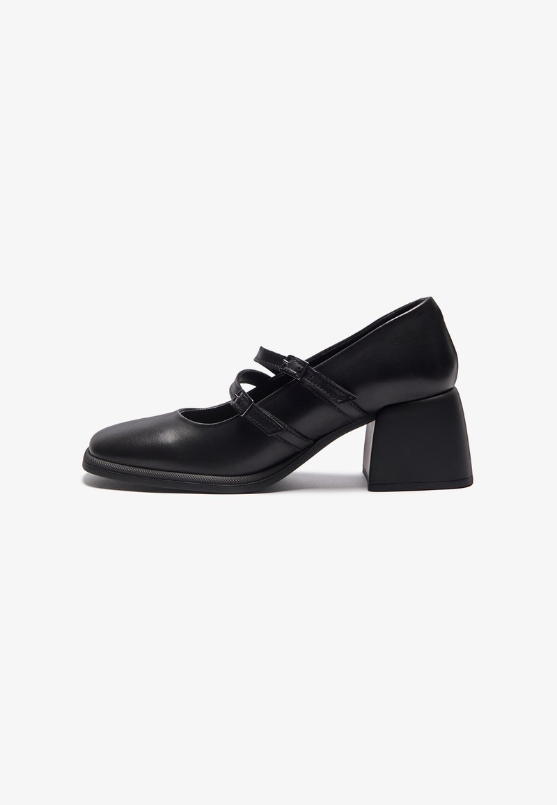 Chaussure en cuir noir avec un bout arrondi, des côtés découpés et deux brides réglables. Dotée d'un talon épais et géométrique pour plus de stabilité.